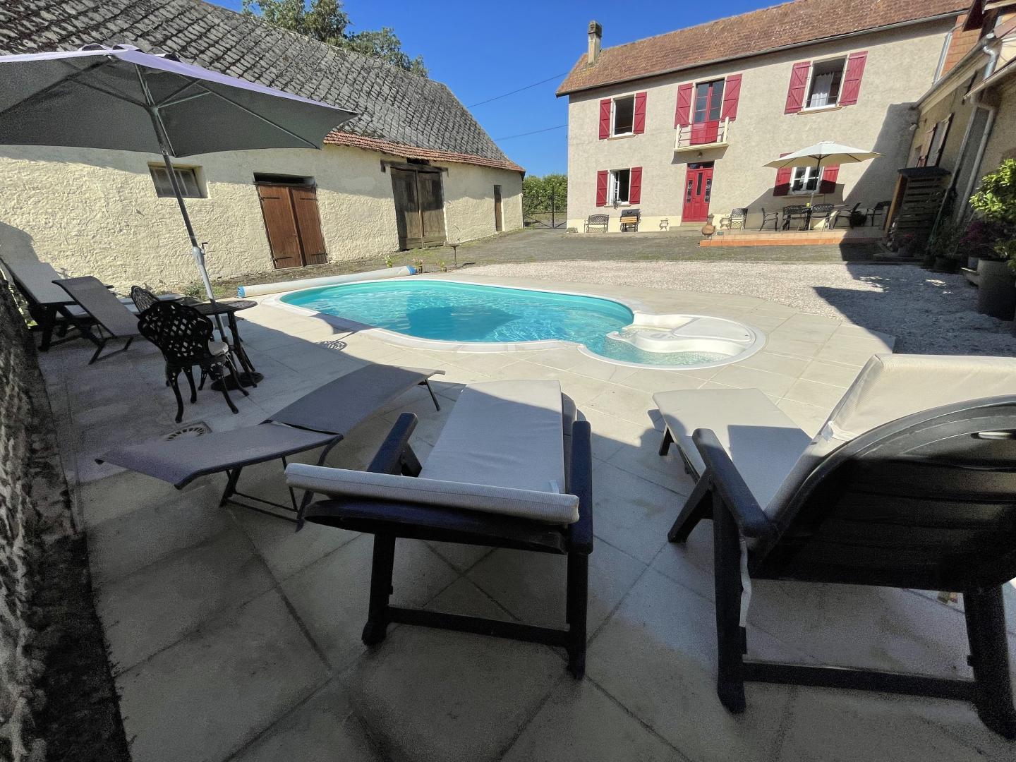 Pool terrace with sun loungers and view of Maison Lajus stone farmhouse with red shutters, Bassillon-Vauzé, Pyrénées-Atlantiques