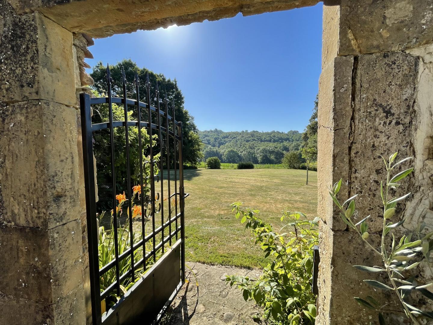 Stone archway and ornamental iron gate opening onto the lawned grounds at Maison Lajus, South West France