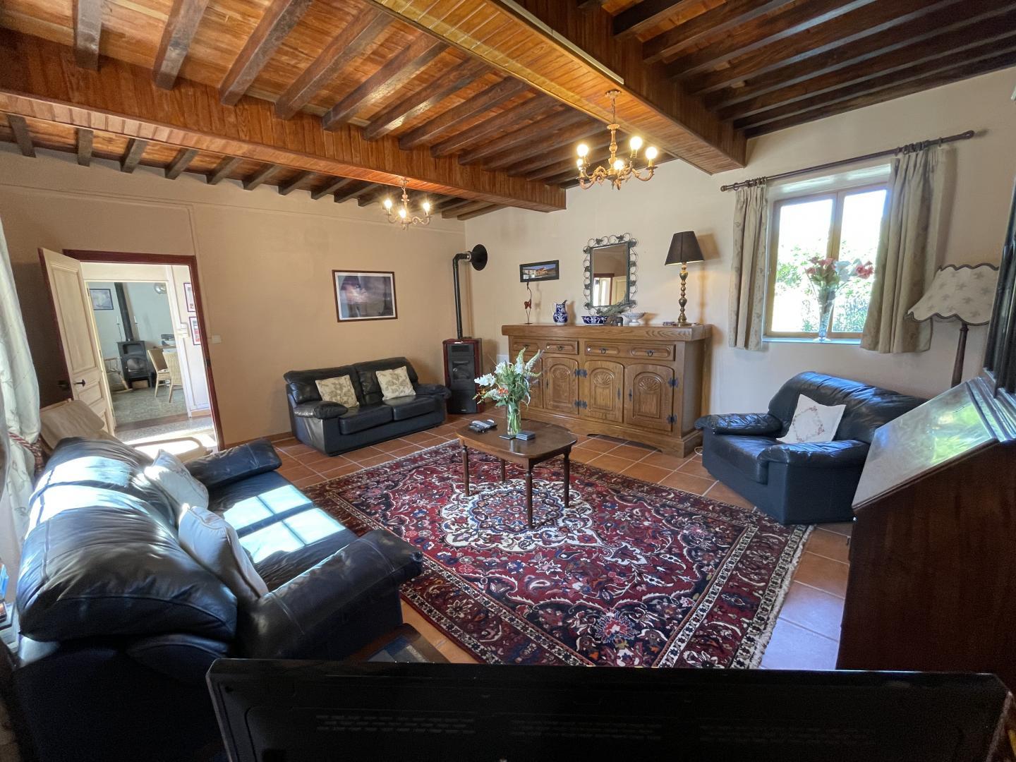 Spacious living room with beamed ceiling, leather sofas and wood-burning stove at Maison Lajus farmhouse gîte, Pyrénées-Atlantiques