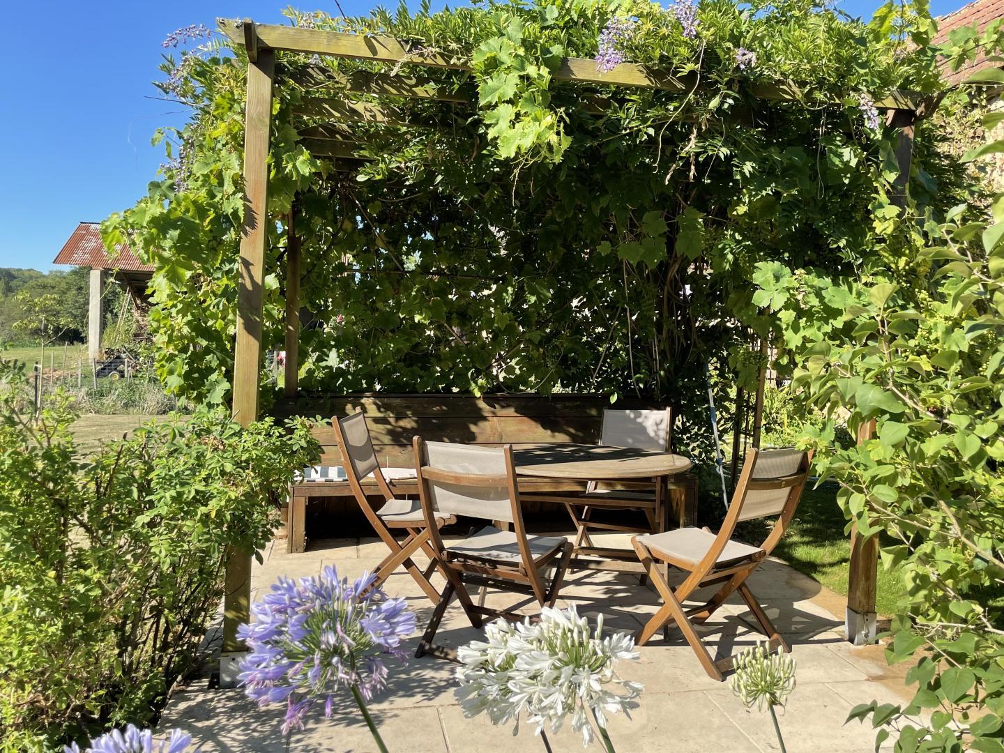 Outdoor dining table and chairs under a wisteria-covered pergola at Maison Lajus holiday gîte, Pyrénées-Atlantiques