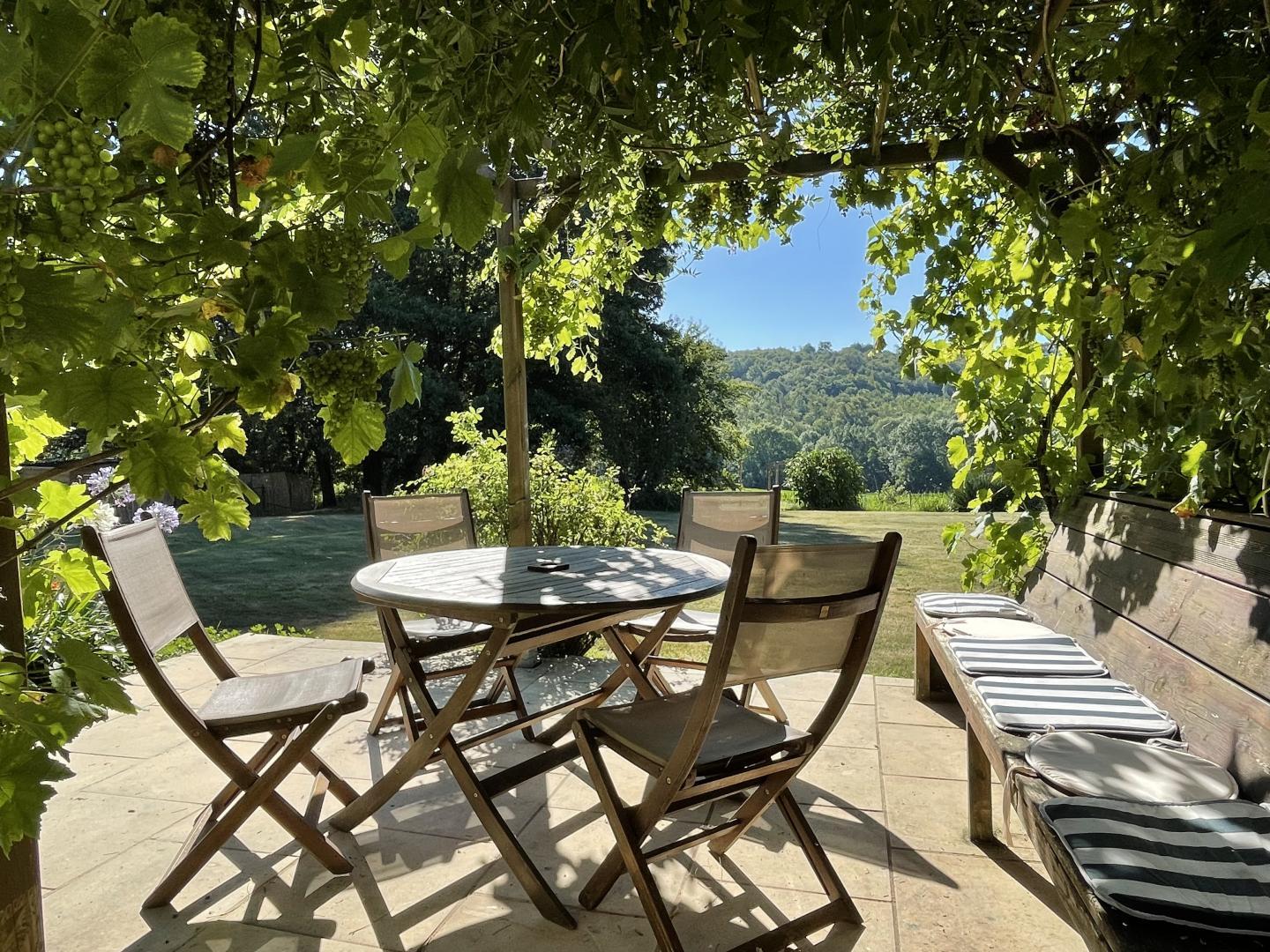 Outdoor patio dining table under a vine pergola with countryside views at Maison Lajus holiday gîte, Pyrénées-Atlantiques