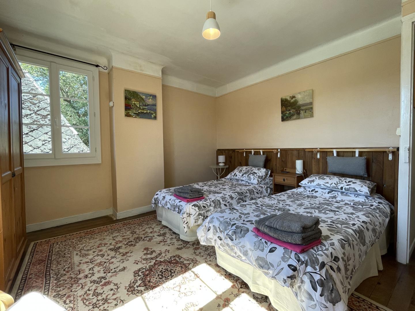 Twin bedroom with two single beds, wooden headboard and garden window at Maison Lajus holiday gîte, South West France